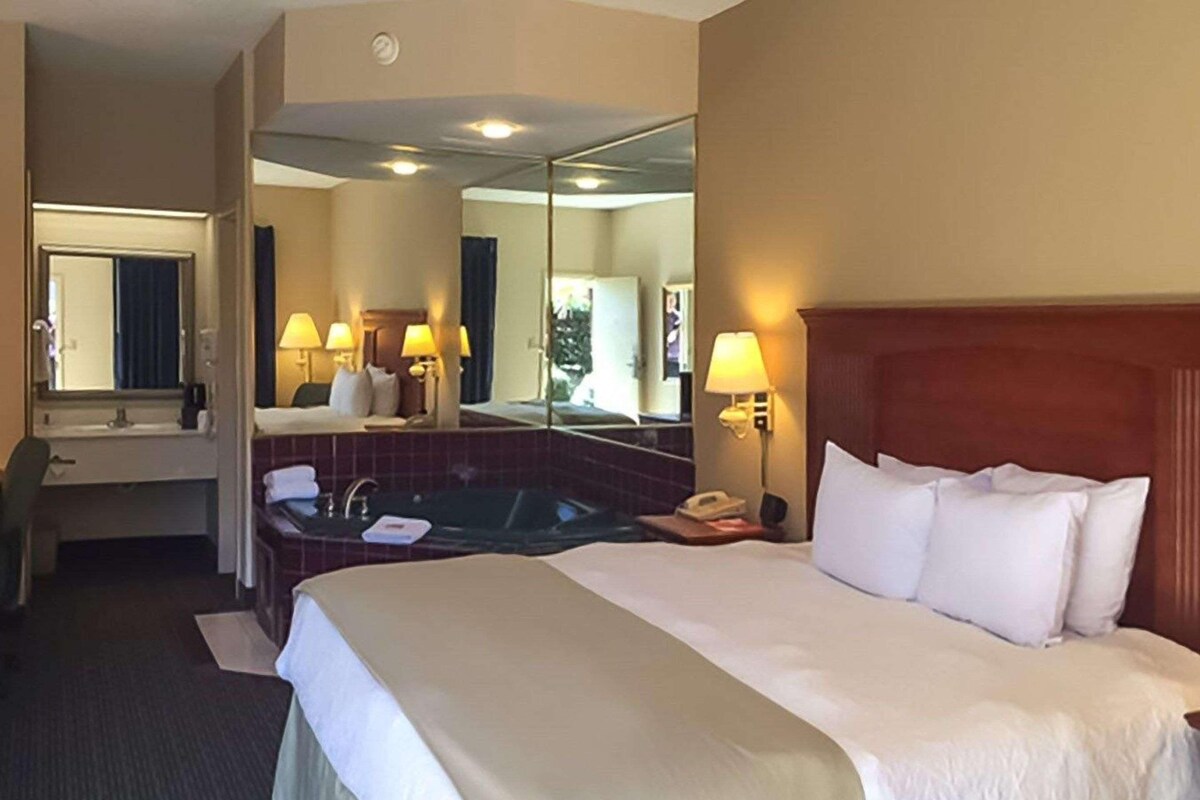 Habitación de hotel con una cama grande, baño independiente con bañera, escritorio y espejo.