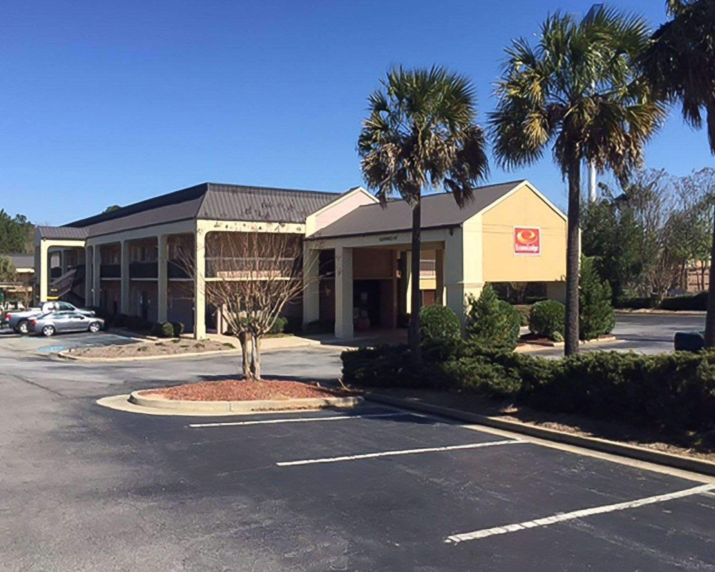 A building with a large parking lot, palm trees, and a sign with a red logo.