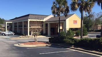 A building with a large parking lot, palm trees, and a sign with a red logo.