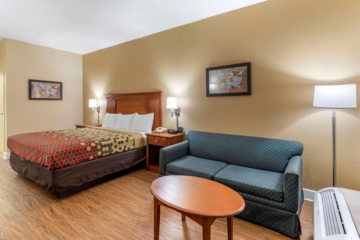 Ein Hotelzimmer mit Bett, einer Couch, einem kleinen Tisch und einem Heizlüfter.