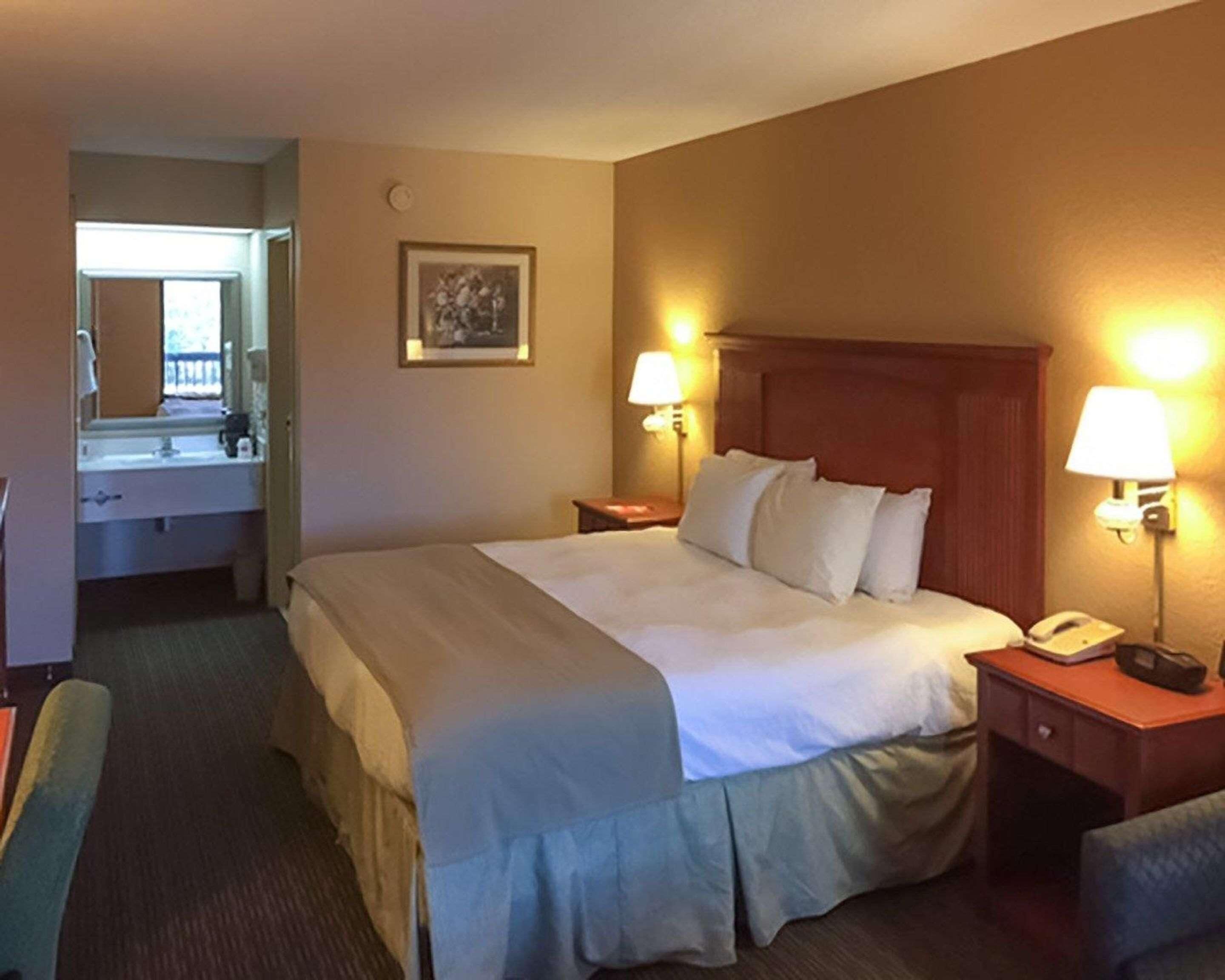 A hotel room with a bed, bedside lamps, a telephone, a mirror, and a picture on the wall.