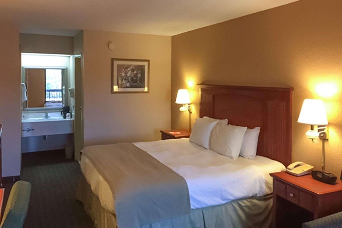 Habitación de hotel con cama, lámparas de noche, teléfono, espejo y un cuadro en la pared.