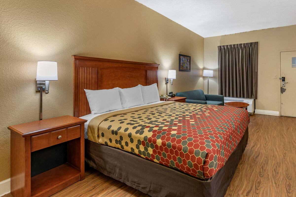 Ein Hotelzimmer mit einem Bett, Nachttischen, einem Schreibtisch, einem Sessel, einer Lampe und einer Tür.