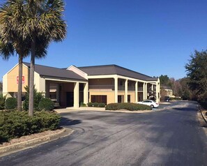 A hotel with a covered parking area, a single-story building, and a palm tree in the foreground. - Econo Lodge Cordele (Cordele)