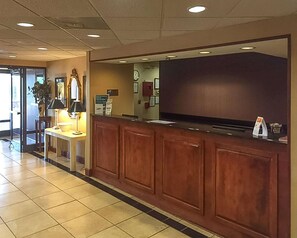 A reception area with a wooden counter, a flat-screen TV, and a desk with a lamp. - Econo Lodge Cordele (Cordele)