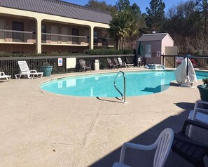 A swimming pool with lounge chairs, a lifeguard stand, and a building with balconies in the background.