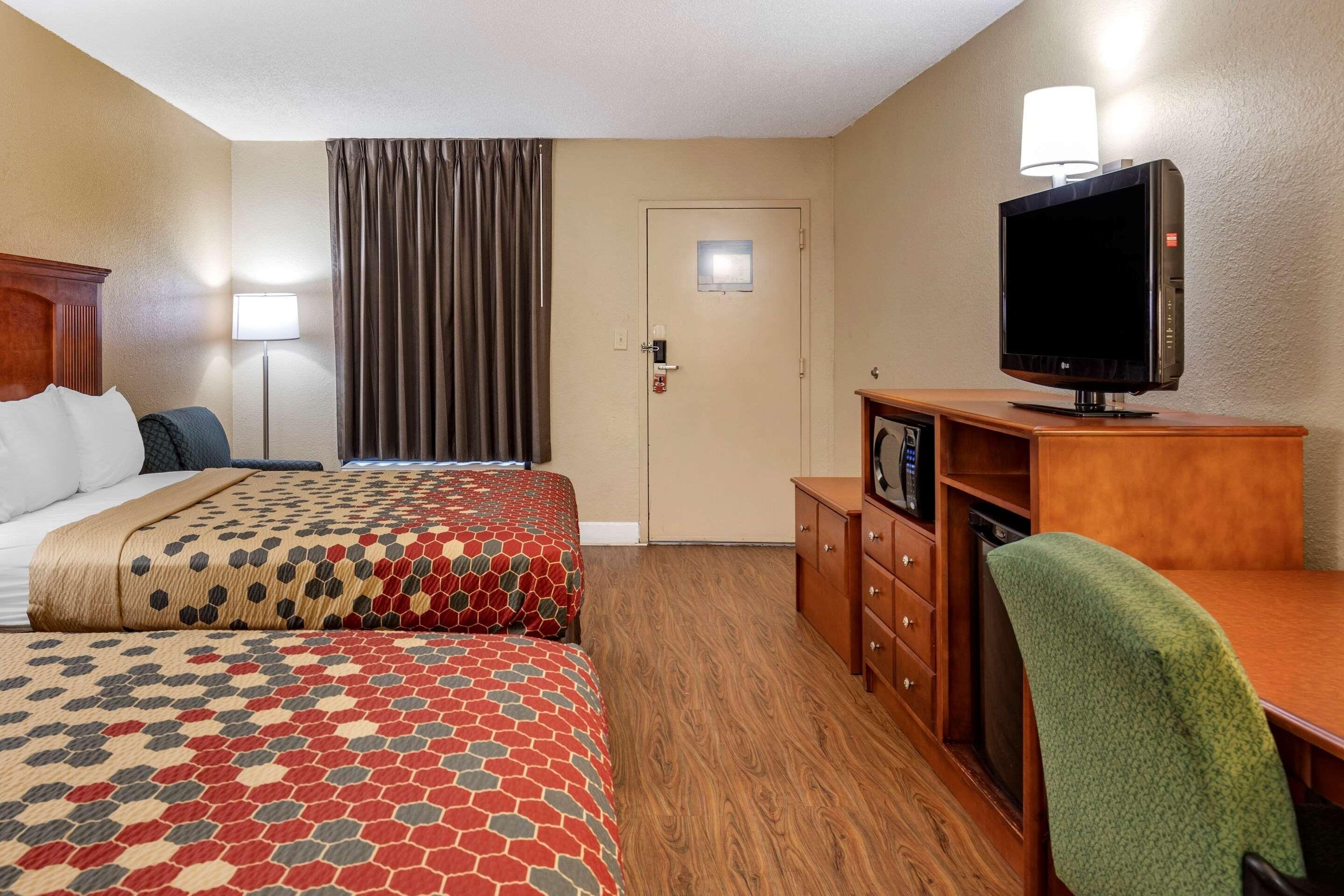 A hotel room with two beds, a television, a desk, and a chair.