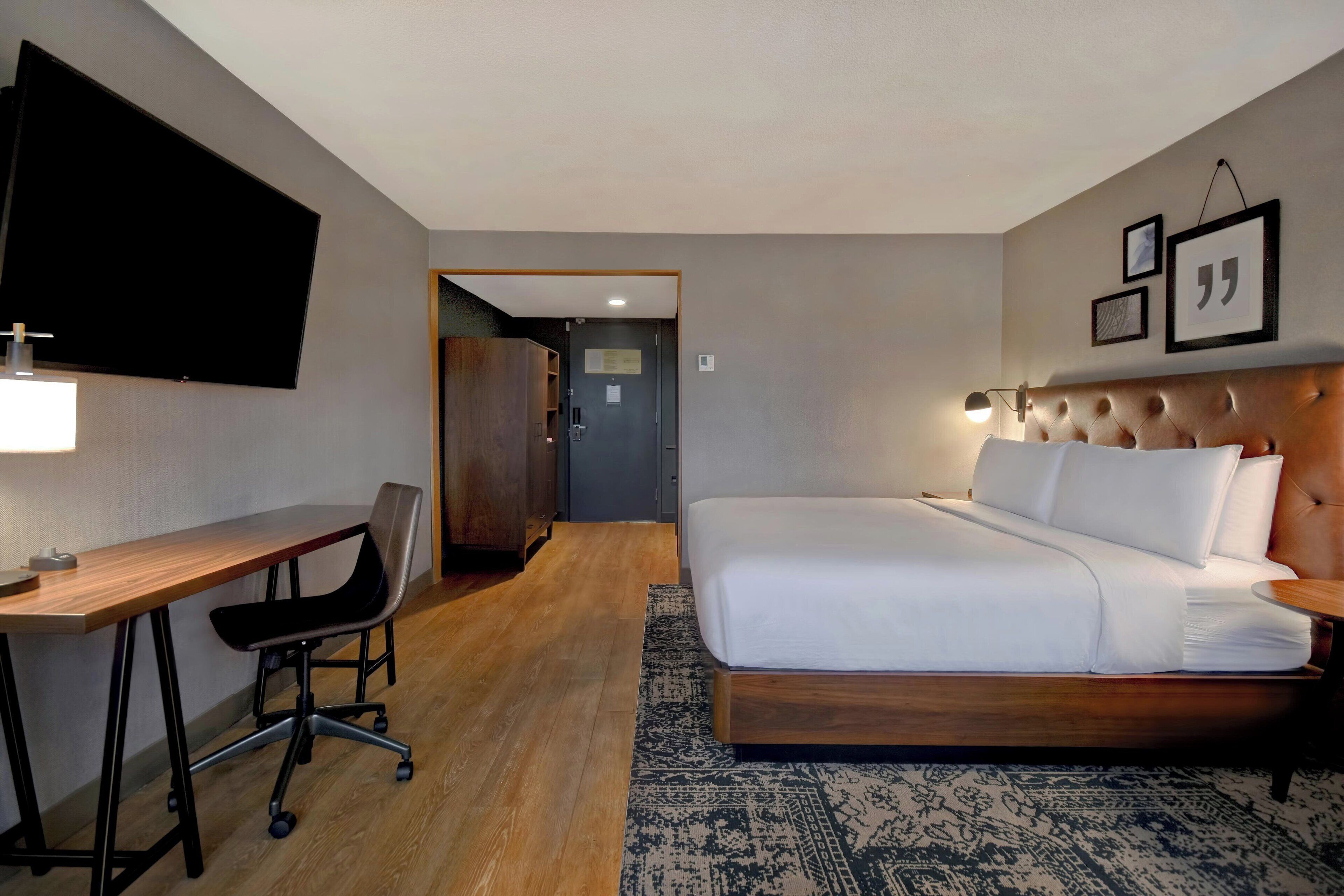 Habitación de hotel con cama, escritorio, silla y televisor de pantalla plana montado en la pared.