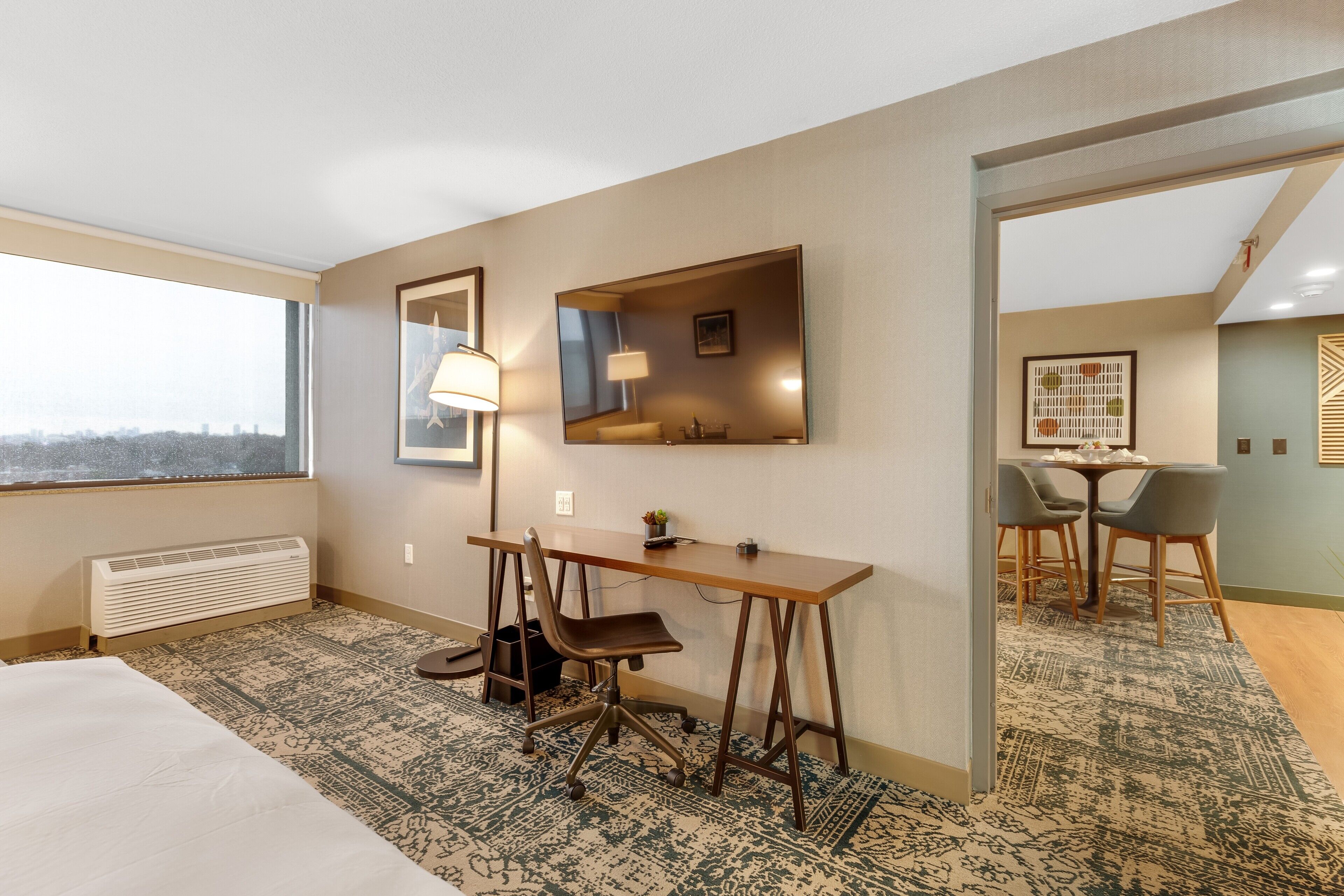 Ein Hotelzimmer mit Bett, Schreibtisch, Stuhl und einem großen Fenster.