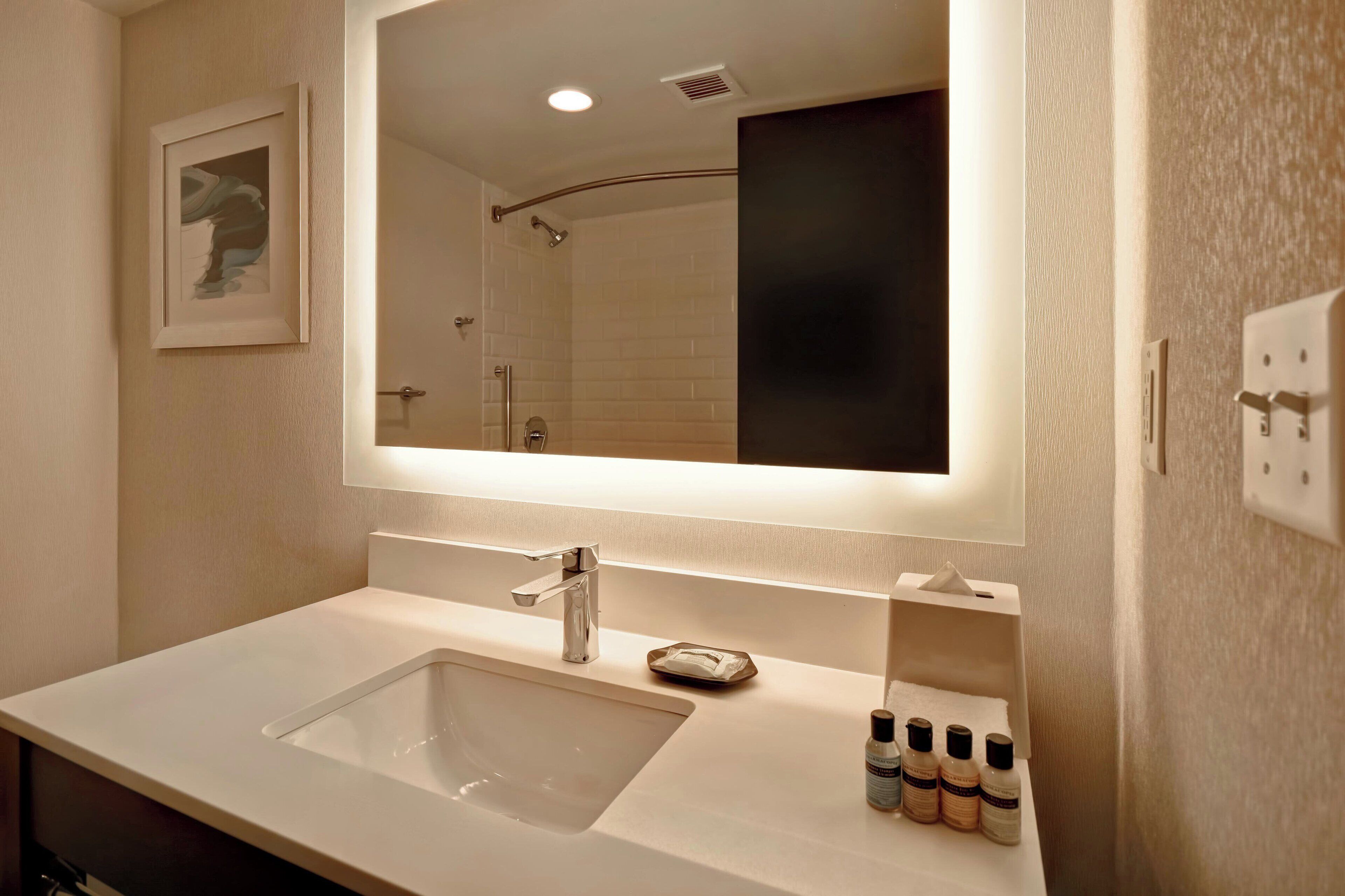 Un baño moderno con un espejo grande, un lavamanos y una ducha.