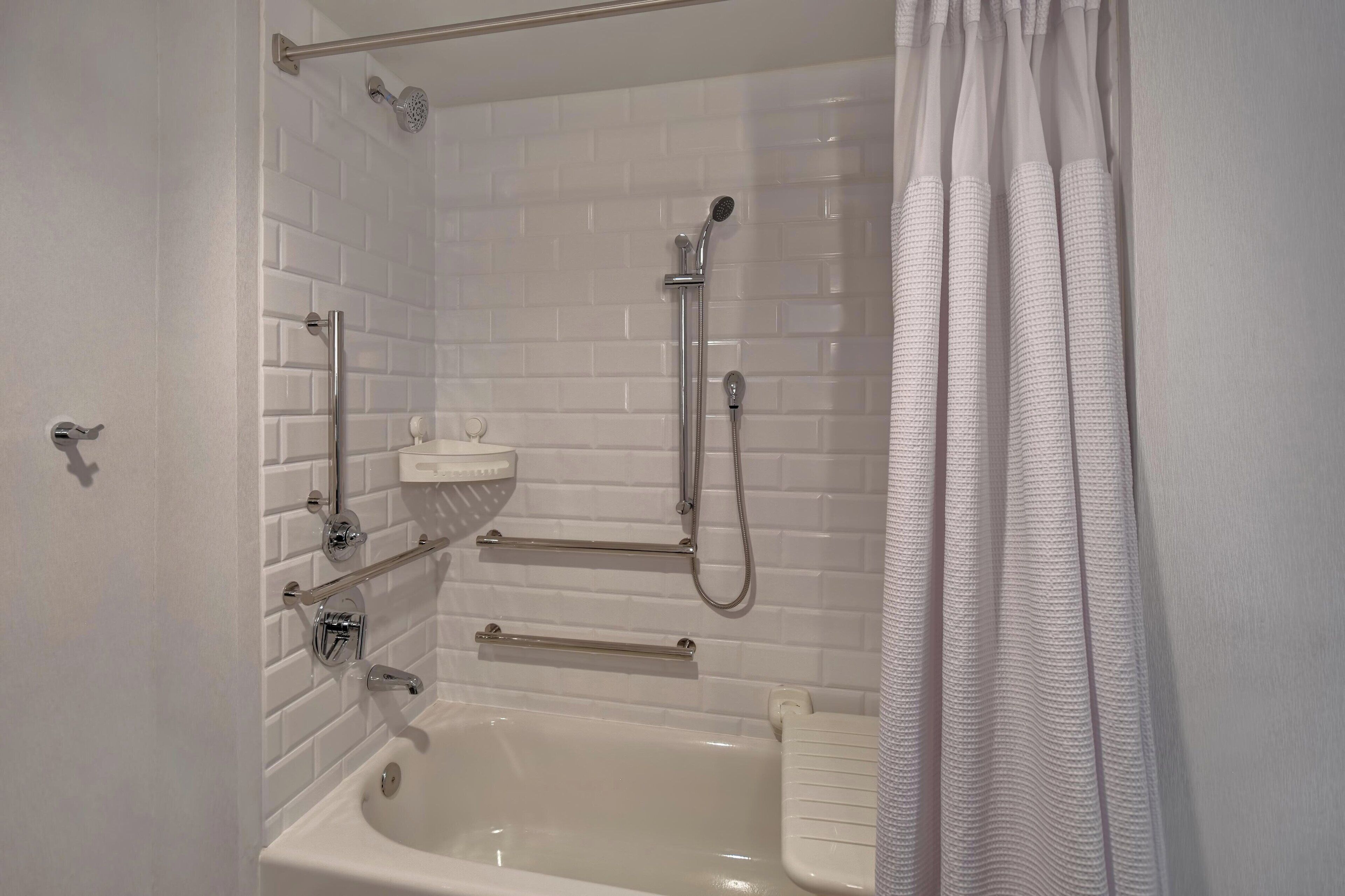 Un baño moderno con paredes de azulejos tipo metro blancos, una bañera blanca, un cabezal de ducha manual y un lavabo blanco con un jabonero.