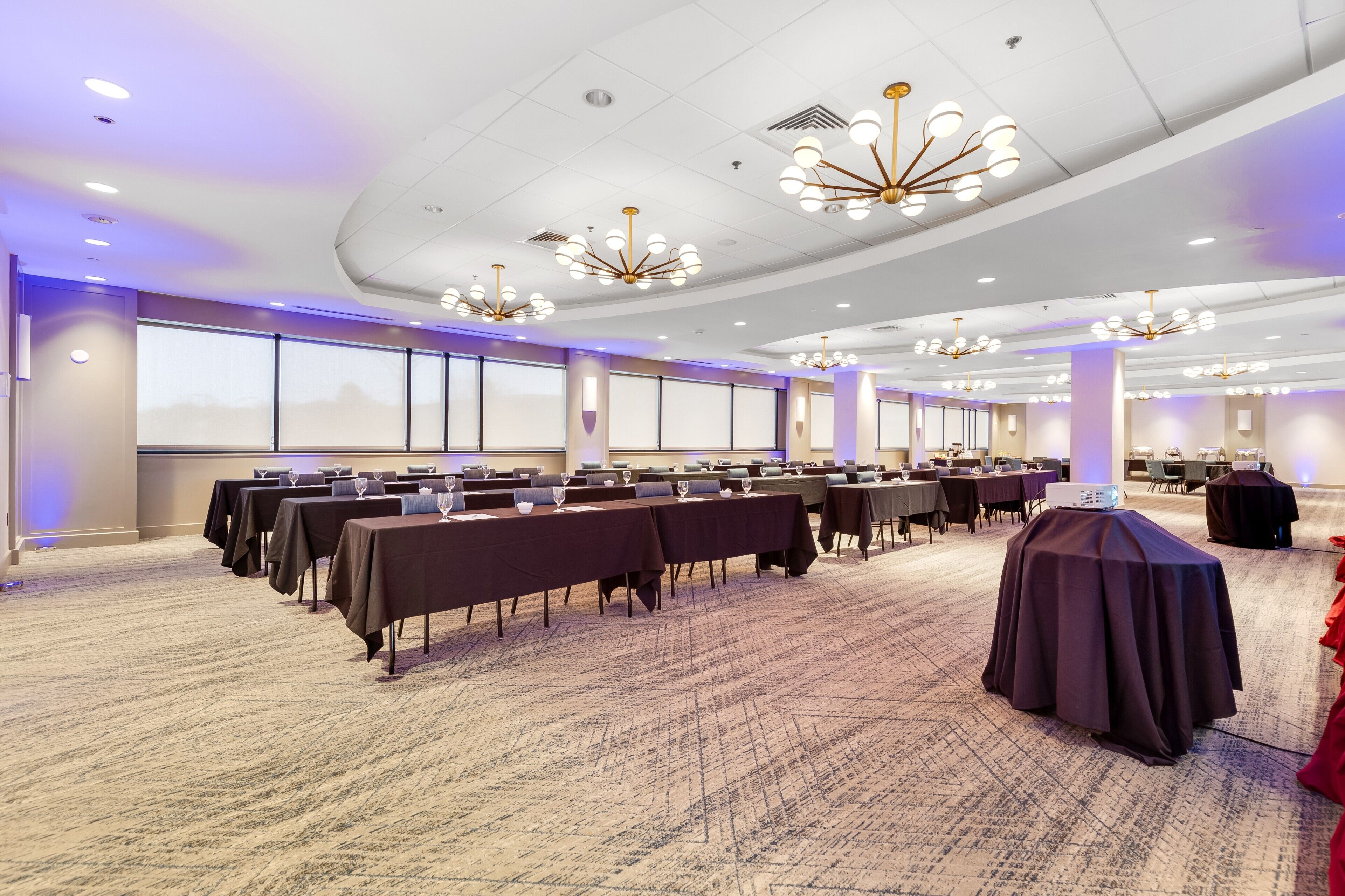 A conference room with rows of tables, ceiling lights, and large windows.
