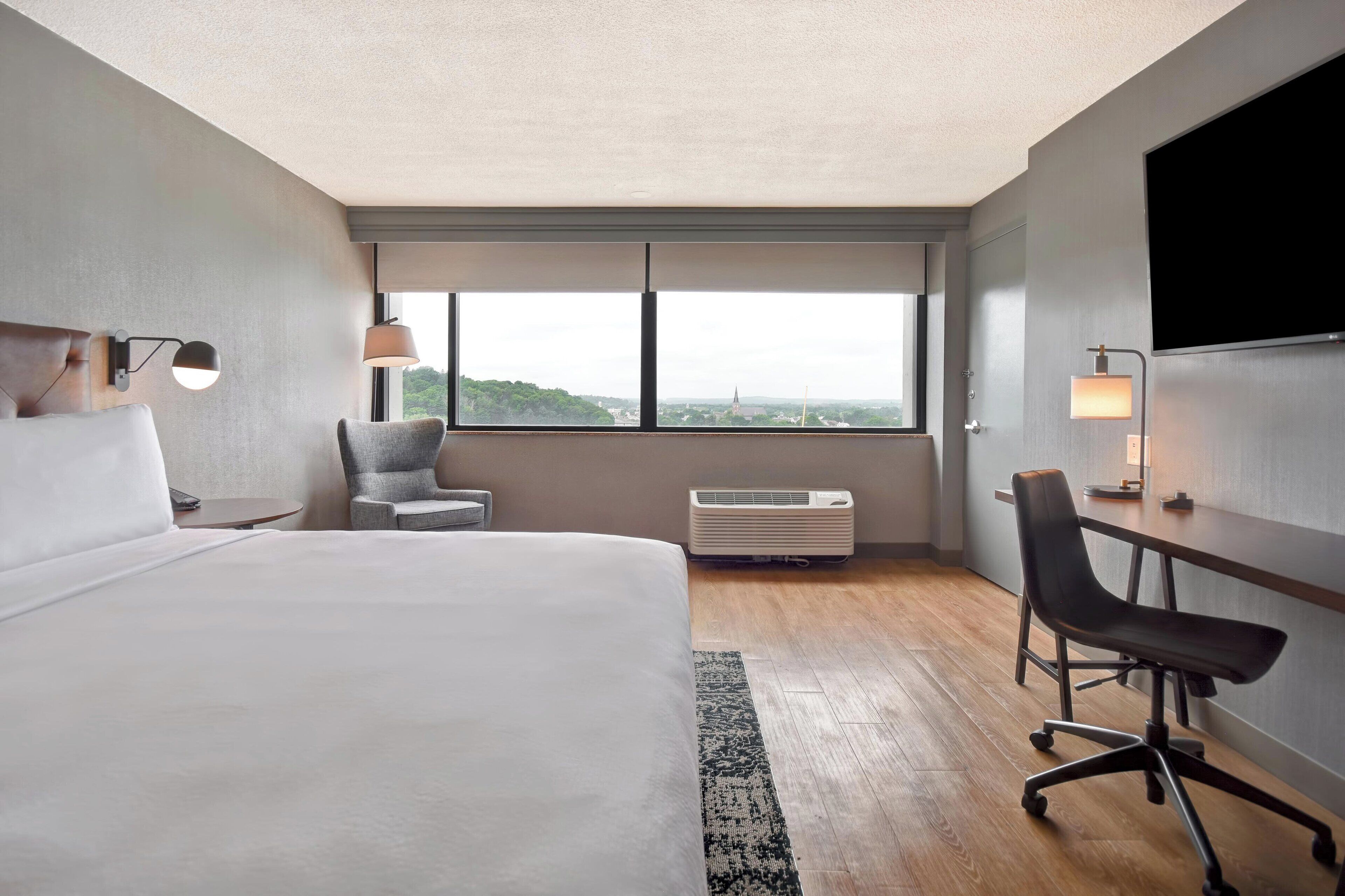 Une chambre d’hôtel avec un grand lit, un bureau, une chaise, une télévision et une fenêtre donnant sur la ville.