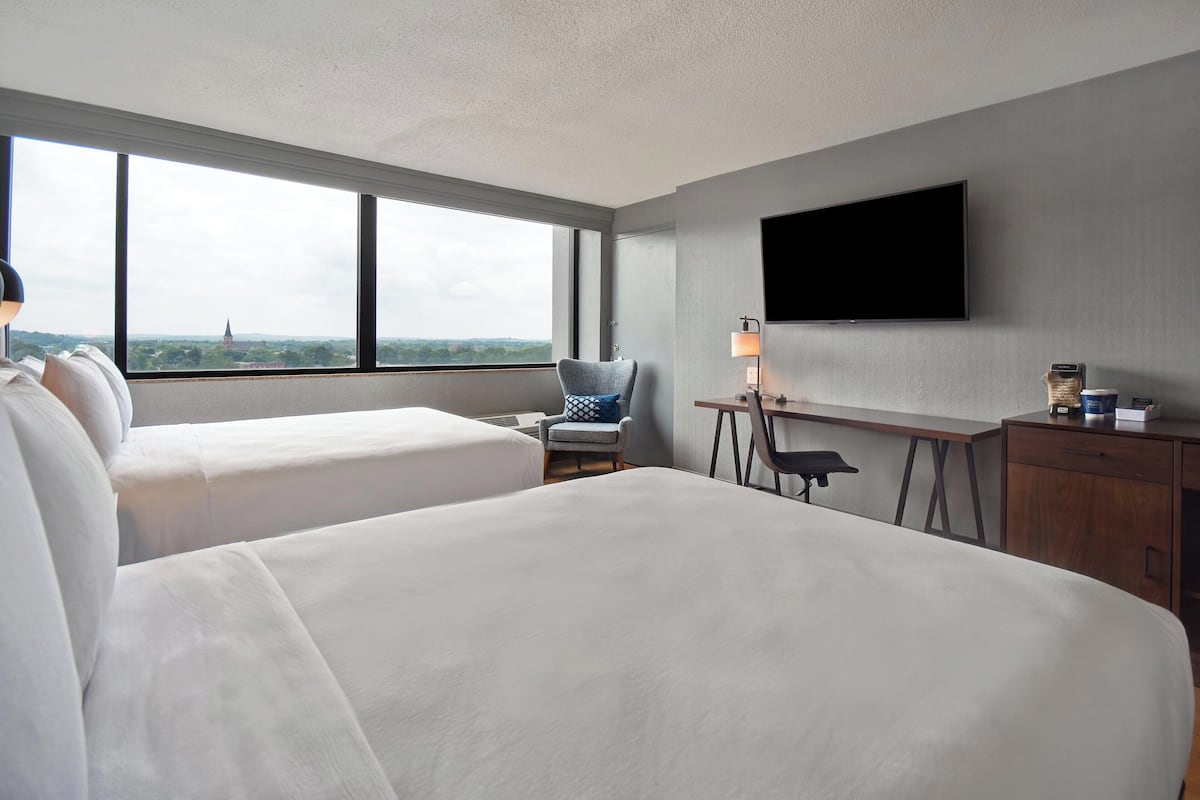 Ett hotellrum med två sängar, ett skrivbord, en stol, en TV och utsikt över stadsbilden.