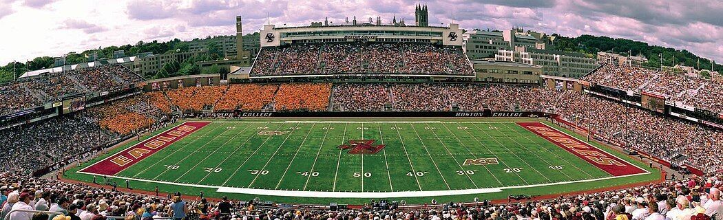 A large stadium with multiple tiers of seating, a football field, and a prominent building with a tower.