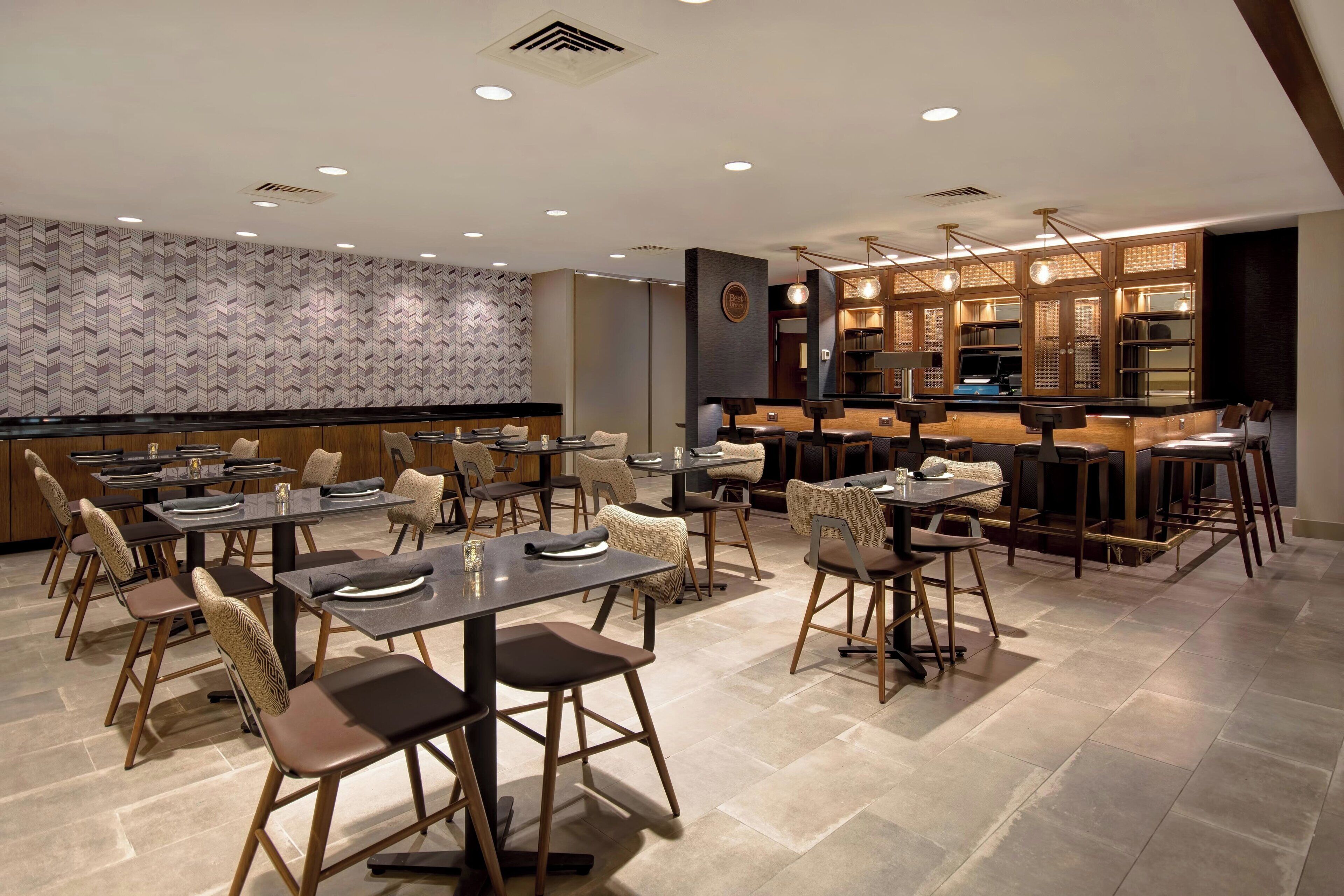 A modern restaurant with multiple dining tables and chairs, a bar area, and a patterned wall.
