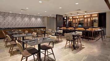 A modern restaurant with multiple dining tables and chairs, a bar area, and a patterned wall.