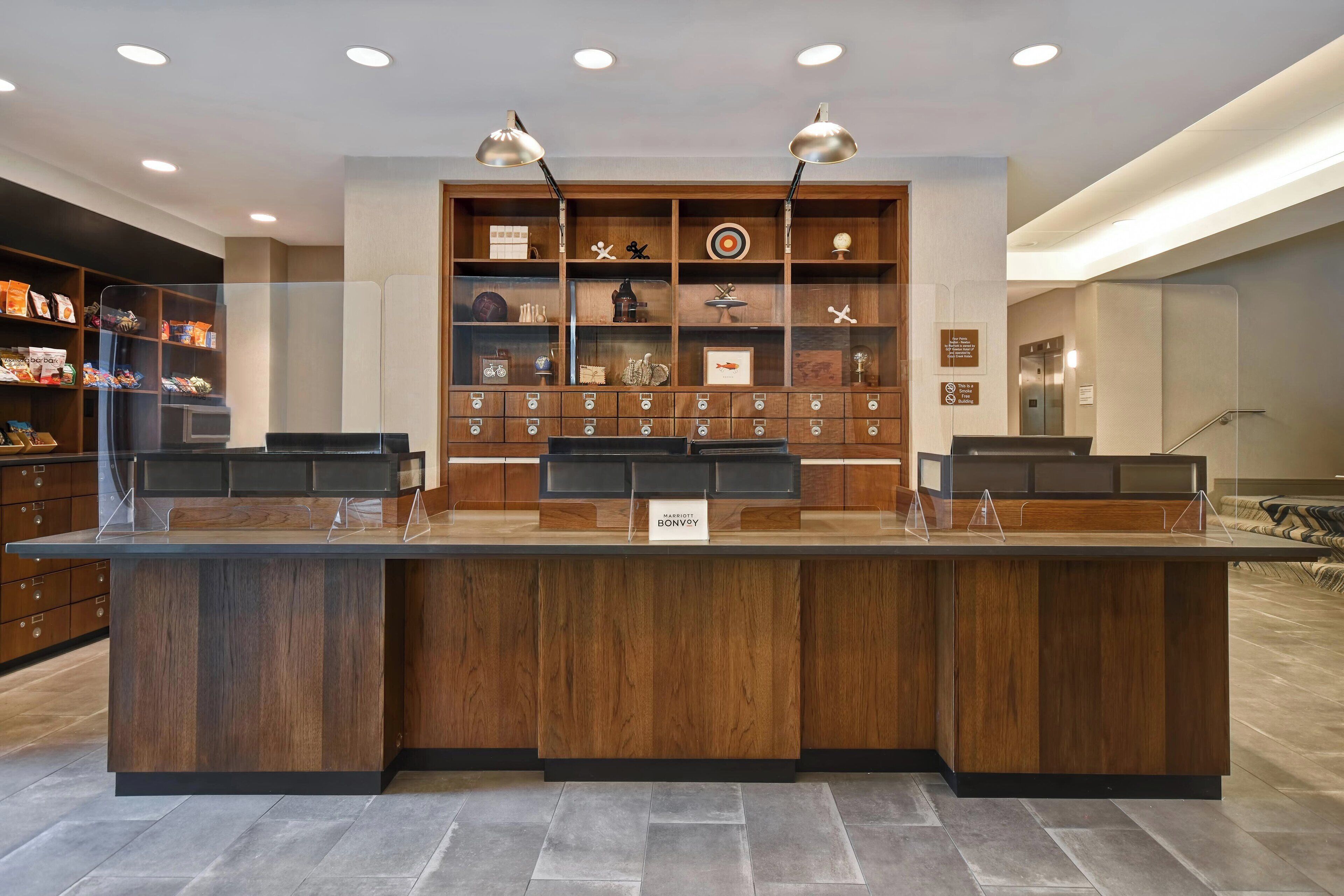 Un mostrador de recepción con detalles de madera, dos lámparas colgantes y una exhibición de varios objetos en estanterías al fondo.