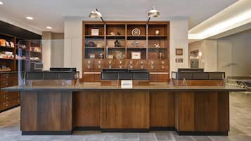 Un mostrador de recepción con detalles de madera, dos lámparas colgantes y una exhibición de varios objetos en estanterías al fondo.