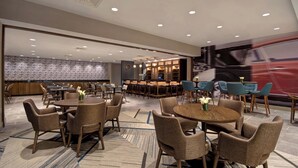 A spacious hotel lobby with multiple seating areas, including round tables and chairs, and a bar area with a counter and stools. - Four Points by Sheraton Boston Newton (Newton)