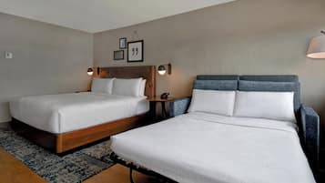 A hotel room with two beds, a small table, and a wall-mounted lamp.