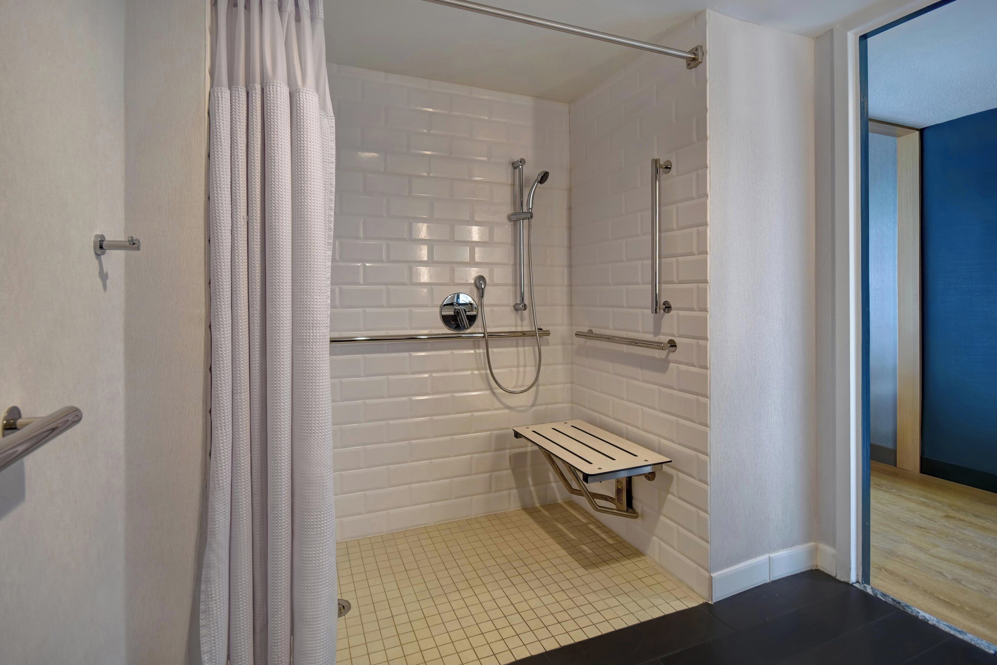 Ducha con paredes de azulejos blancos, cabezal de ducha metálico y un pequeño banco.