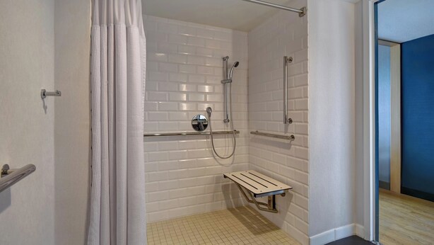 A shower with white tiled walls, a metal showerhead, and a small bench. - Four Points by Sheraton Boston Newton (Newton)