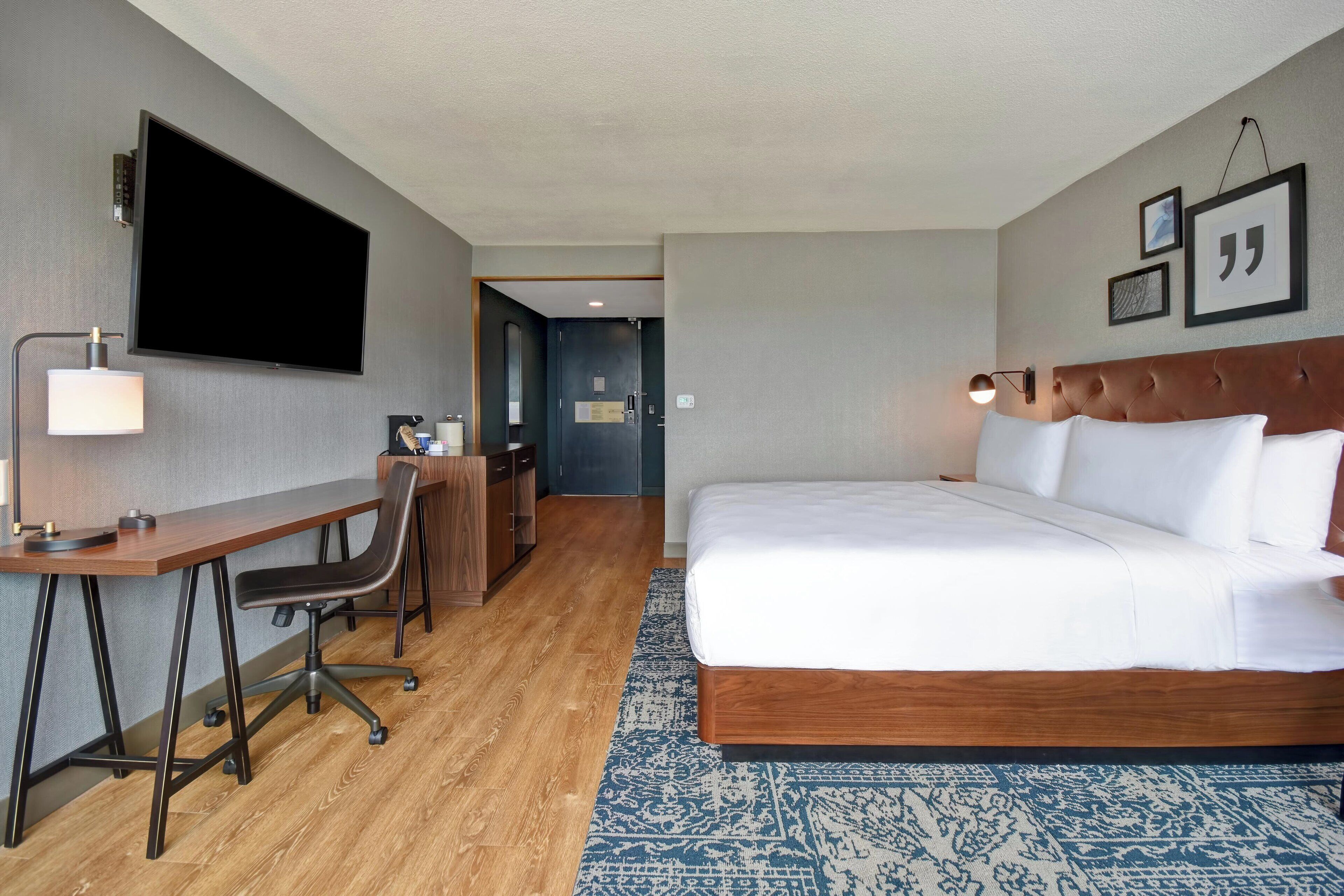 A hotel room with a bed, desk, chair, television, and a door leading to another room.