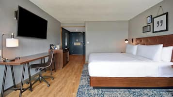 Una camera d'albergo con un letto, una scrivania, una sedia, televisione e una porta che dà su un'altra stanza.