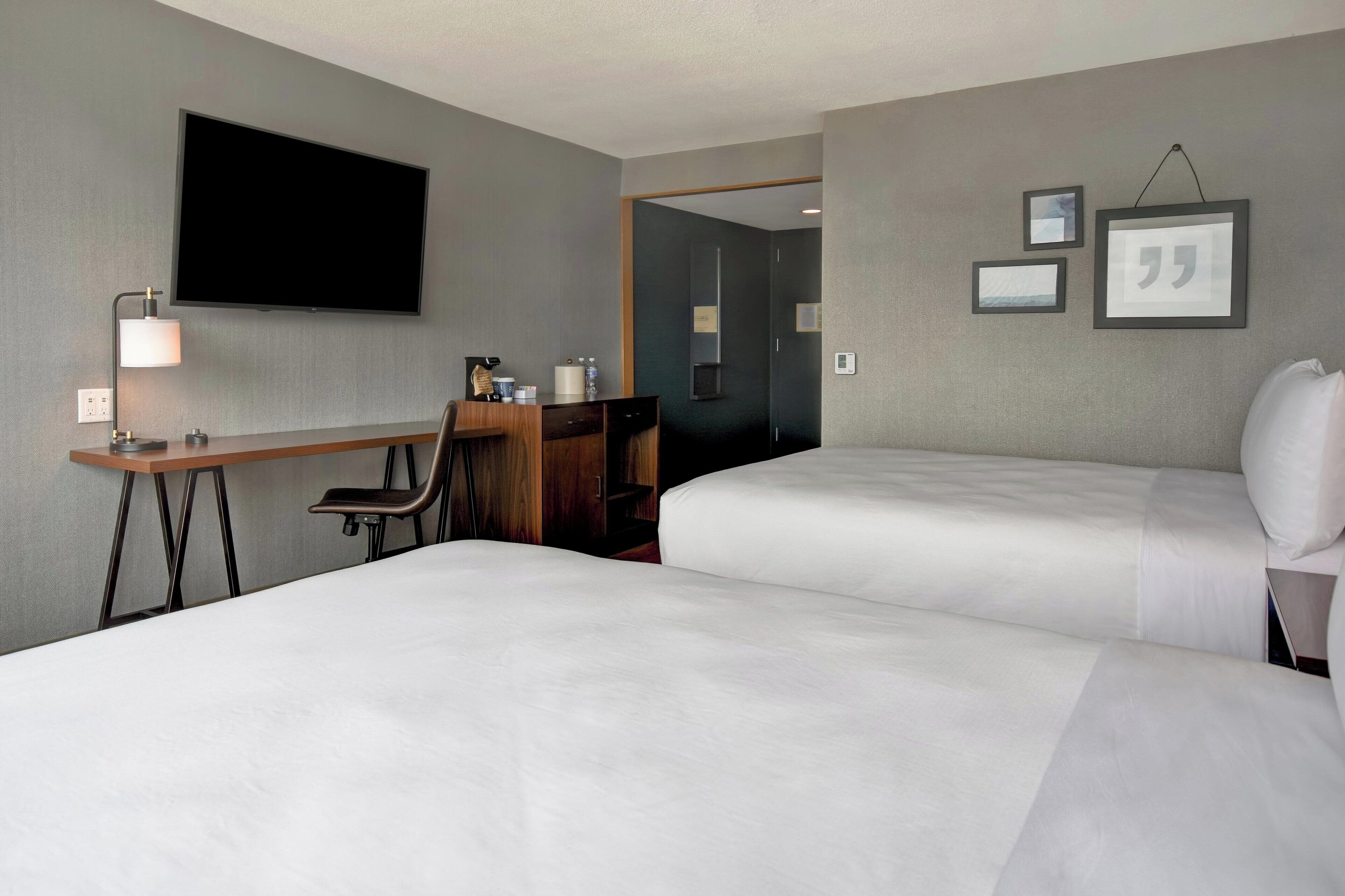 A hotel room with two beds, a desk, a chair, a TV, and framed pictures on the wall.