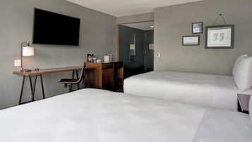 A hotel room with two beds, a desk, a chair, a TV, and framed pictures on the wall.