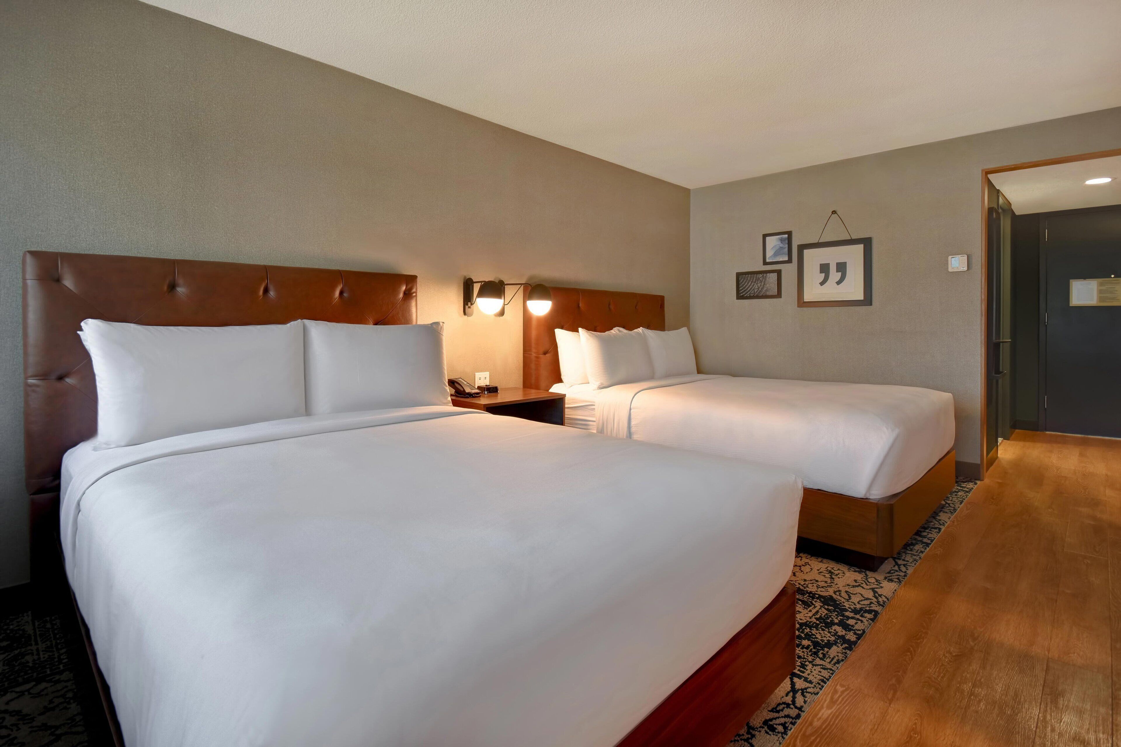 Une chambre d’hôtel avec deux lits, une tête de lit en bois, une table de chevet et un luminaire fixé au mur.