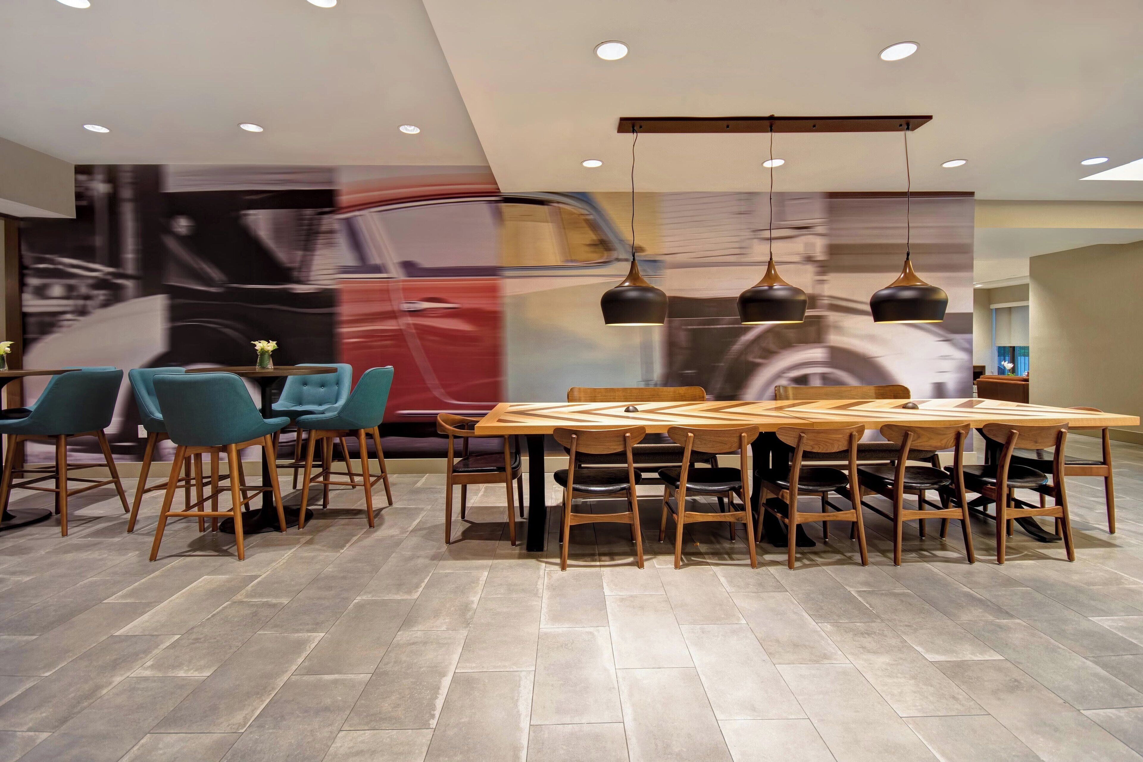 Un comedor moderno con una amplia mesa de madera, sillas color turquesa e iluminación colgante.
