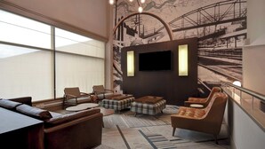 A modern lounge with a large window, comfortable seating, a flat-screen TV, and a map mural on the wall. - Four Points by Sheraton Boston Newton (Newton)