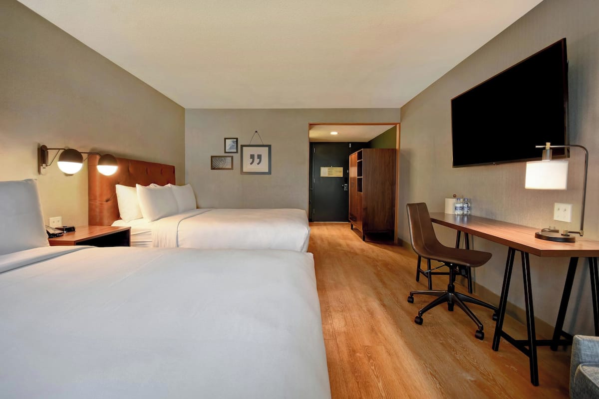 Ett hotellrum med två sängar, ett skrivbord, en stol, en TV och en garderob.