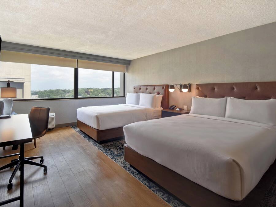 Une chambre d’hôtel avec deux lits, un bureau, une chaise, une télévision et une grande fenêtre donnant sur la ville.