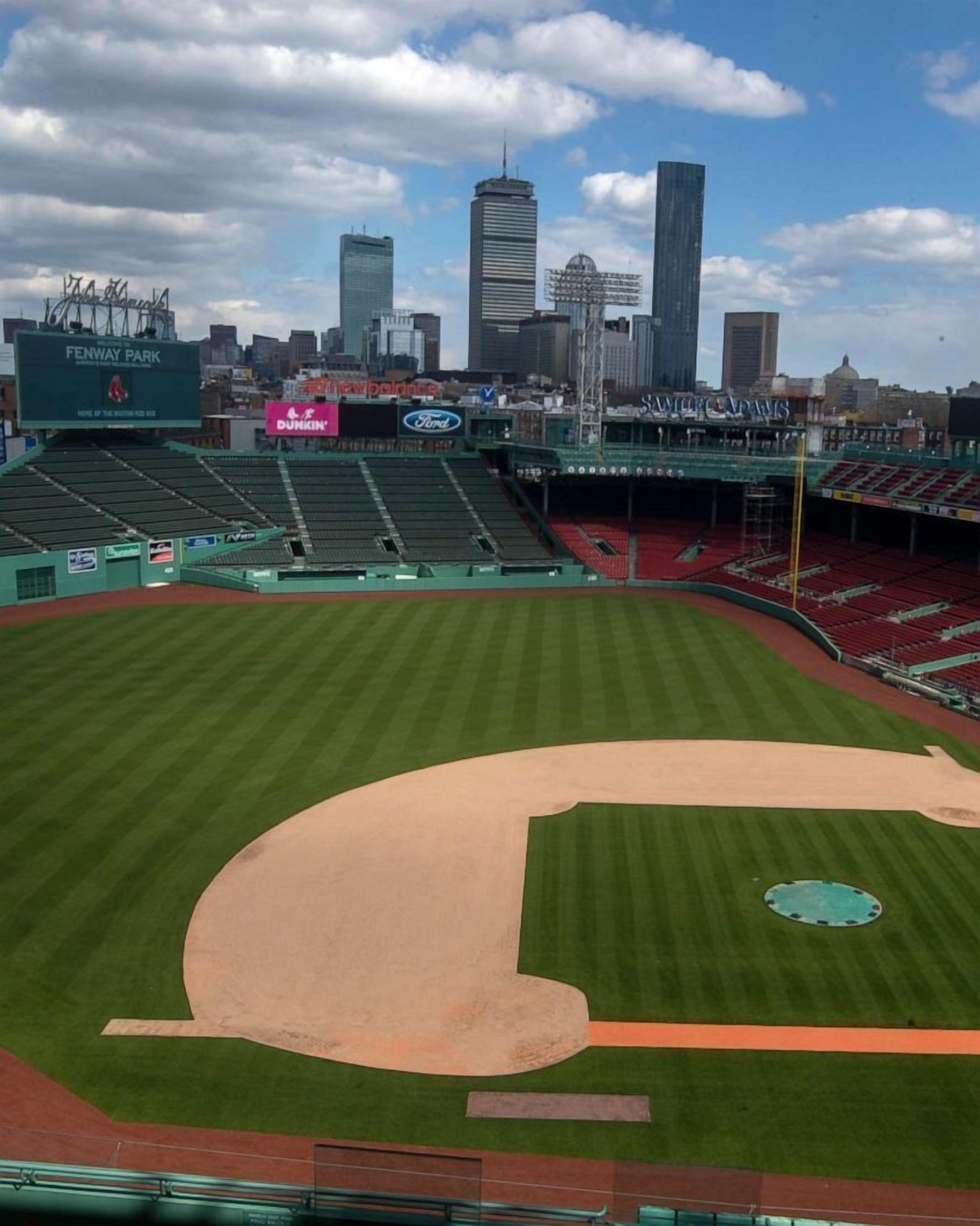 Fenway Park stadion med en baseballbane, grønne sæder og en bysilhuet i baggrunden.