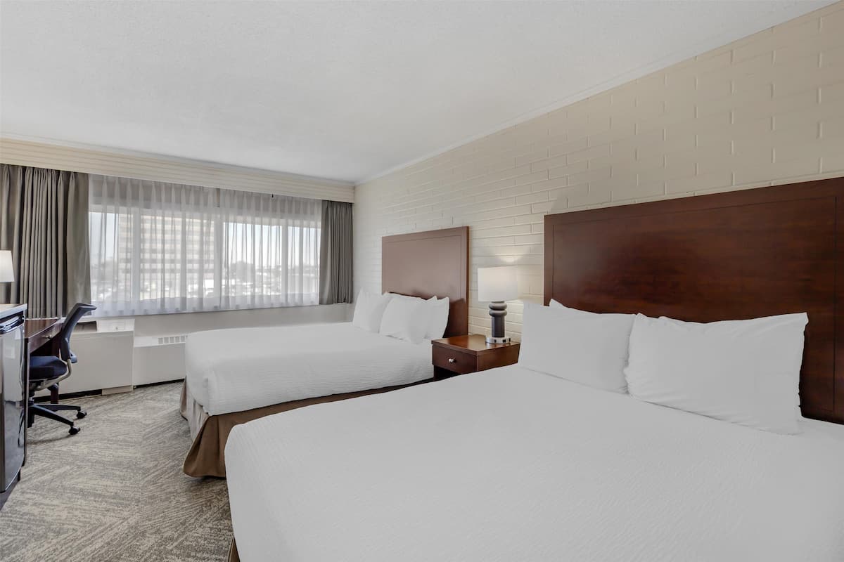 A hotel room with two beds, a desk, and a window with curtains.