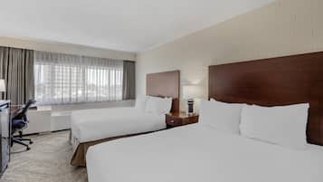 A hotel room with two beds, a desk, and a window with curtains.