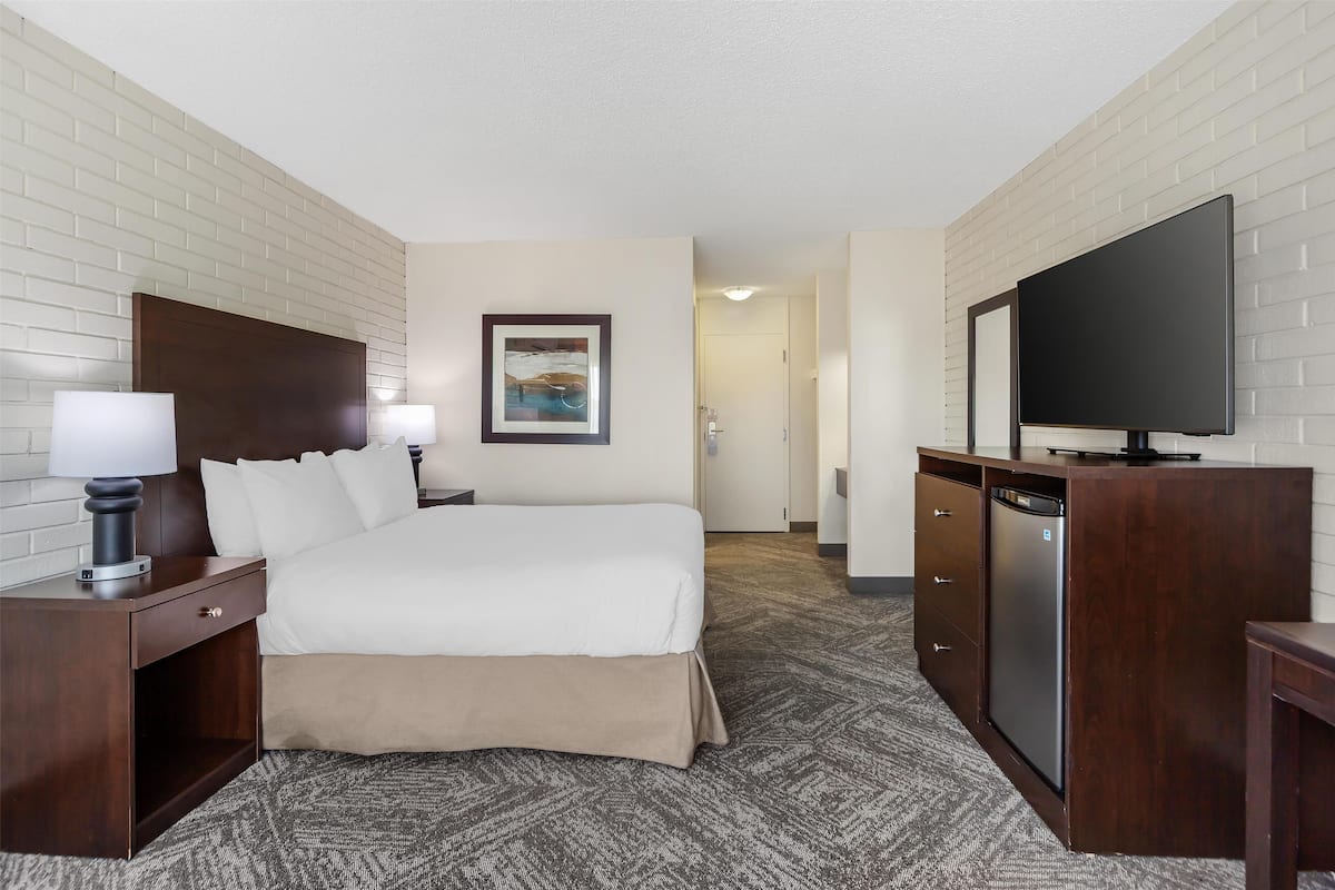 A hotel room with a bed, bedside tables, a TV, and a painting on the wall.