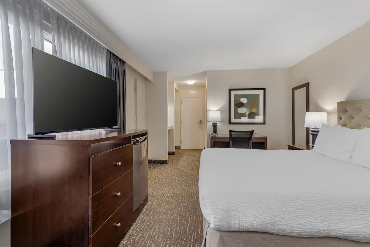 A hotel room with a large bed, a flat-screen TV, a desk with a chair, and a framed artwork on the wall.