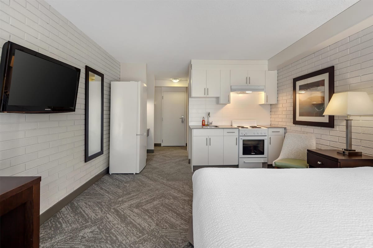 A hotel room with a bed, a TV, a kitchenette, and a bathroom.