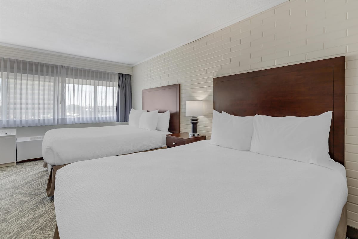 A hotel room with two beds, a desk, and a window with curtains.