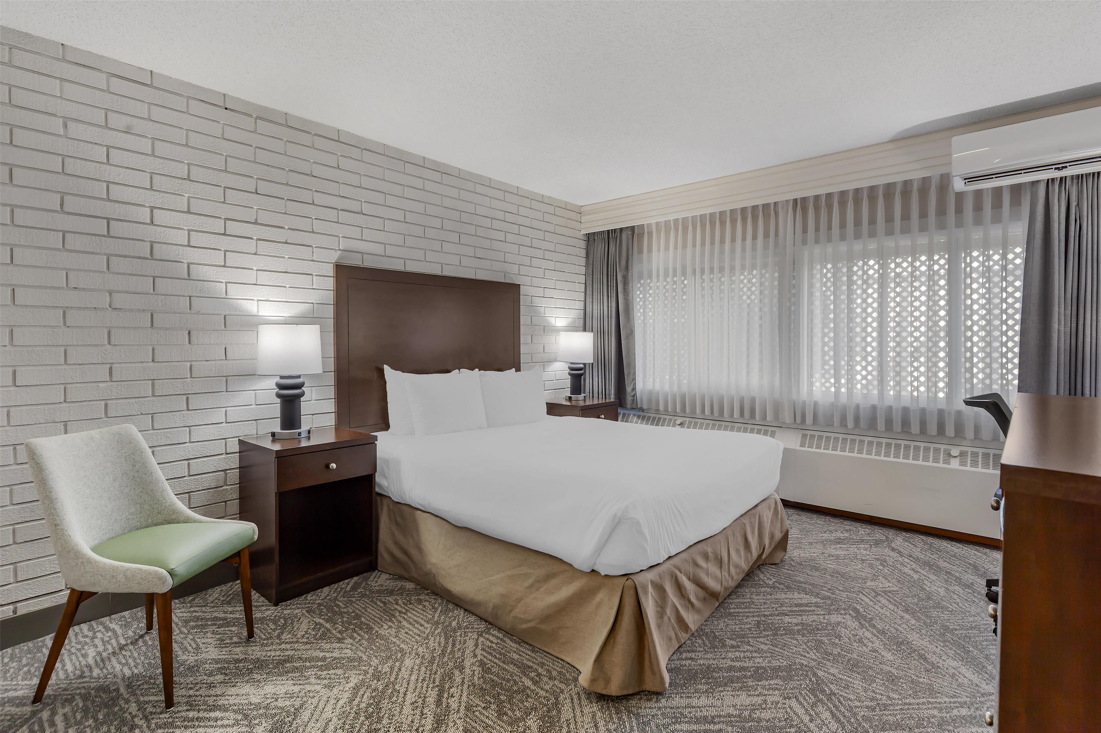 A hotel room with a large bed, a chair, a desk, and a window with curtains.