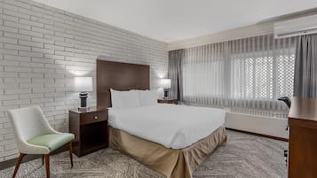 A hotel room with a large bed, a chair, a desk, and a window with curtains.
