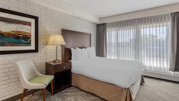 A hotel room with a large bed, a nightstand, a chair, a lamp, a painting on the wall, and a window with curtains.