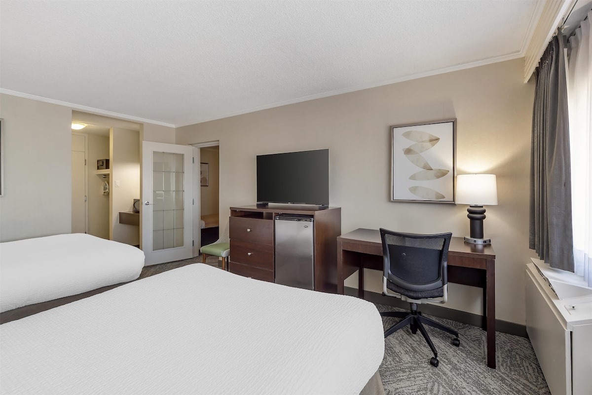 A hotel room with two beds, a desk, a chair, a television, and a lamp.