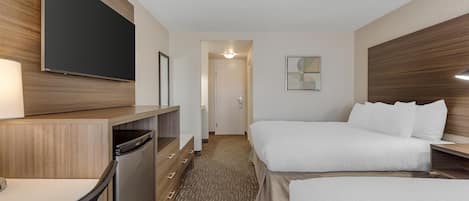 Habitación de hotel con cama, escritorio, televisor de pantalla plana, refrigerador pequeño y puerta que da a un baño.