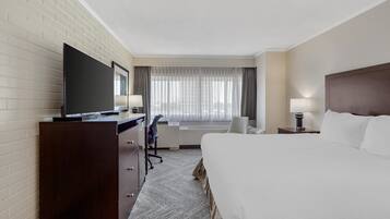 Habitación de hotel con una cama grande, un escritorio con televisor, una silla y una ventana con cortinas.