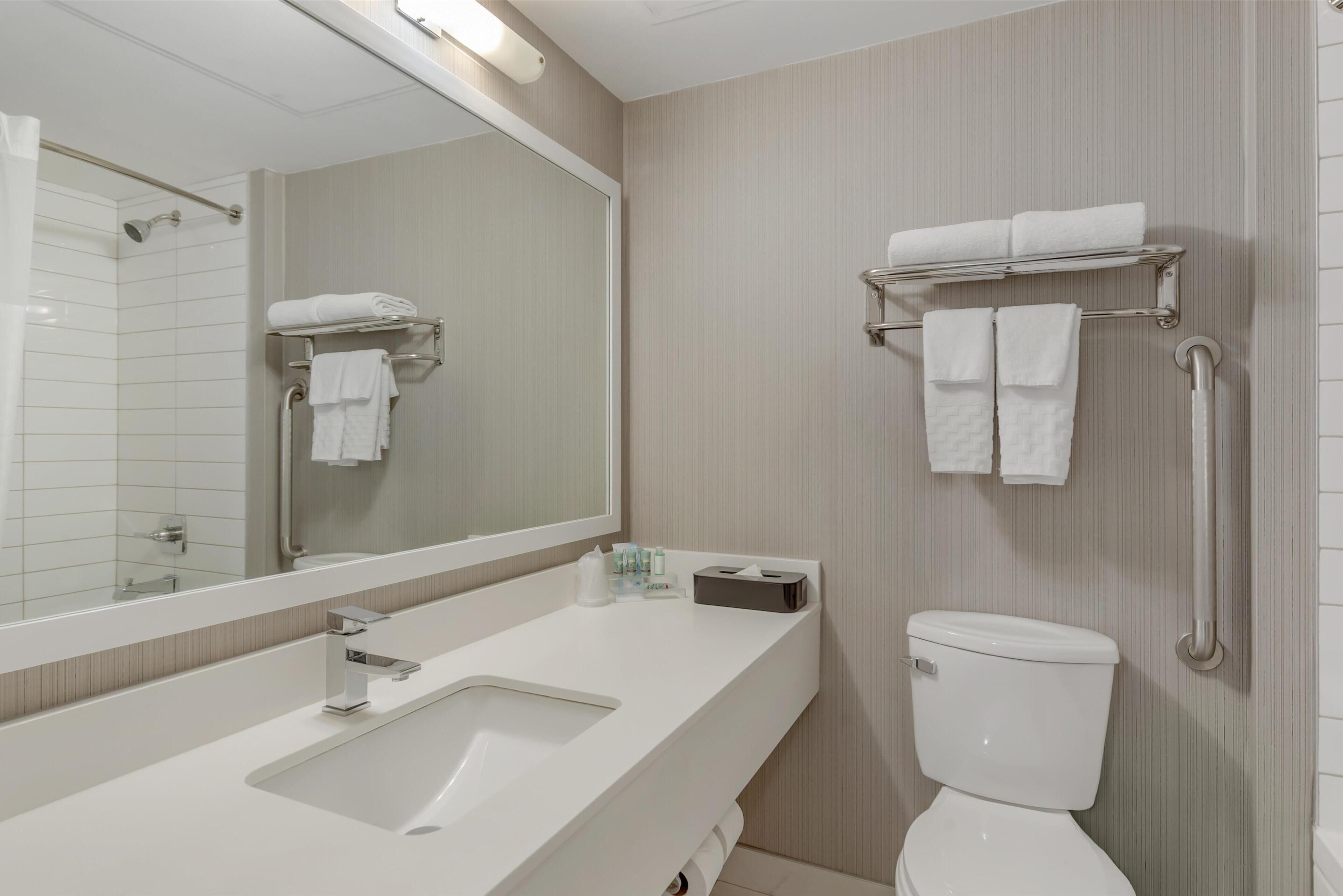 A modern bathroom with a white sink, a mirror, a toilet, and a towel rack.